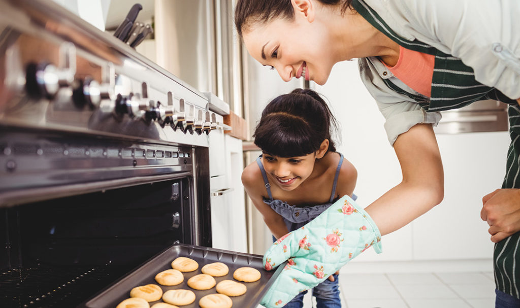 Photo of mother and daughter taking cookies out of the oven