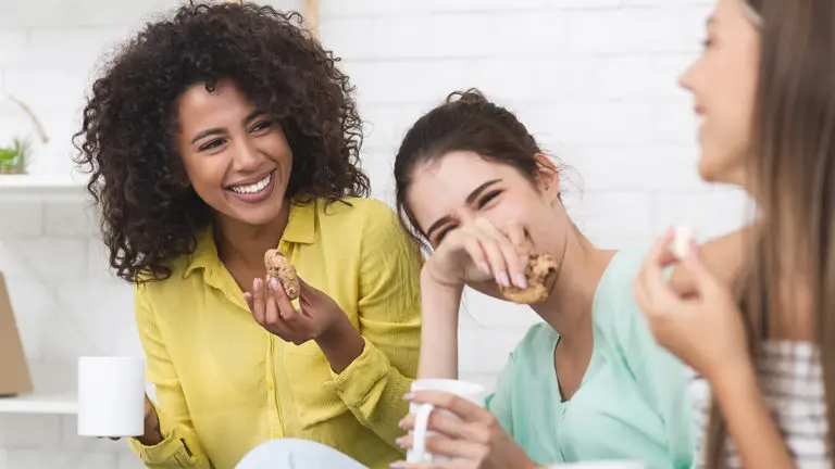 Happy girls drinking tea and eating sweets at home