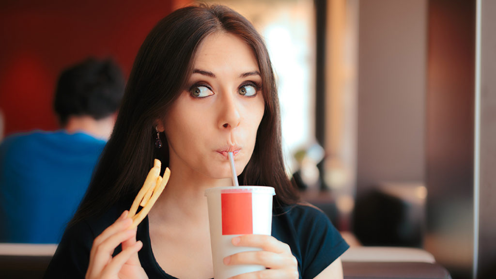 Photo of woman drinking soda and eating fries