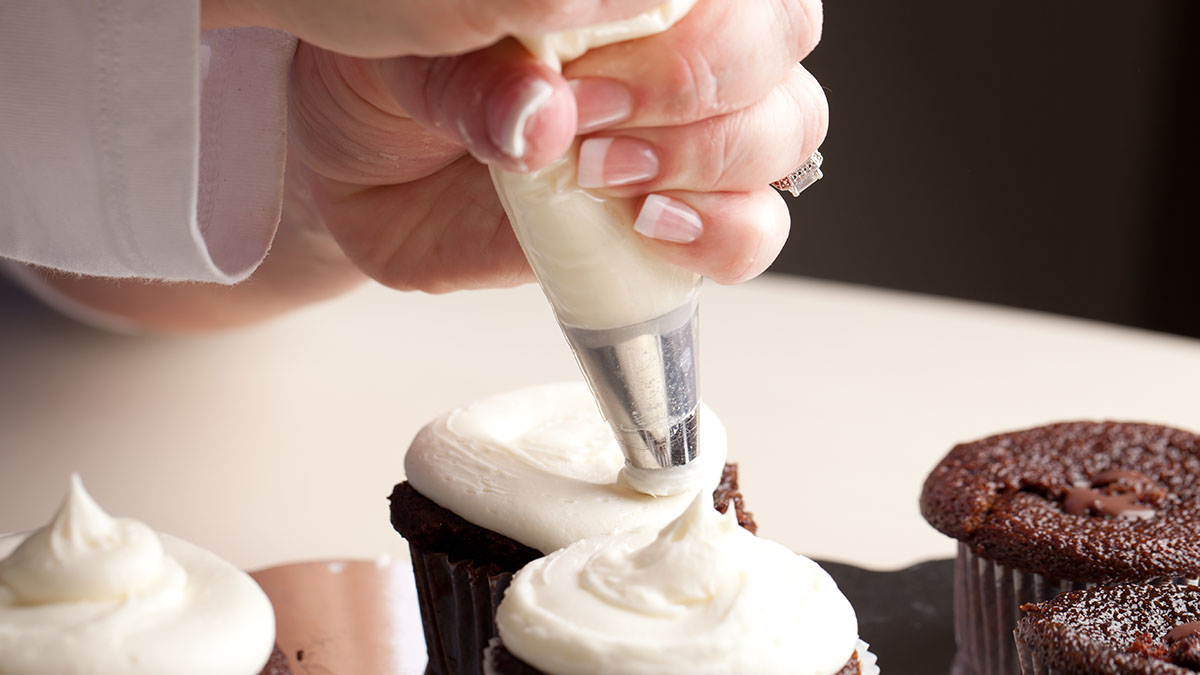 Photo of chef piping buttercream frosting on cupcakes