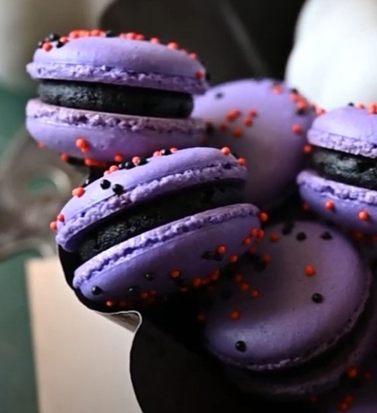 Cookie types with a stack of pumpkin macarons decorated for Halloween.