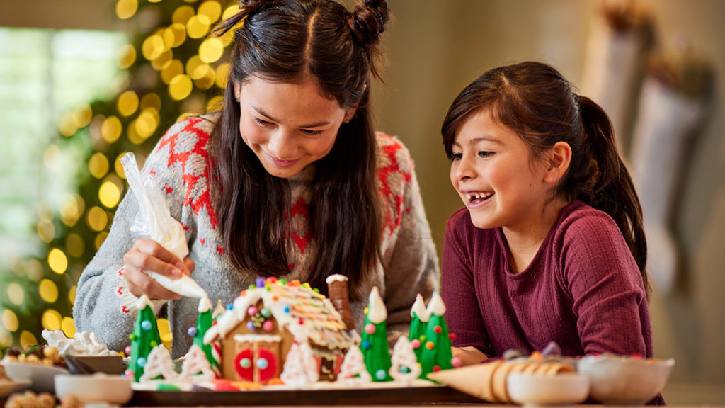 Girls decorating a gingerbread house.