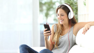Happy girl listening to music from mobile phone sitting on a couch at home