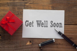 Get Well Soon written on paper with pen,red gift box and wooden background desk.