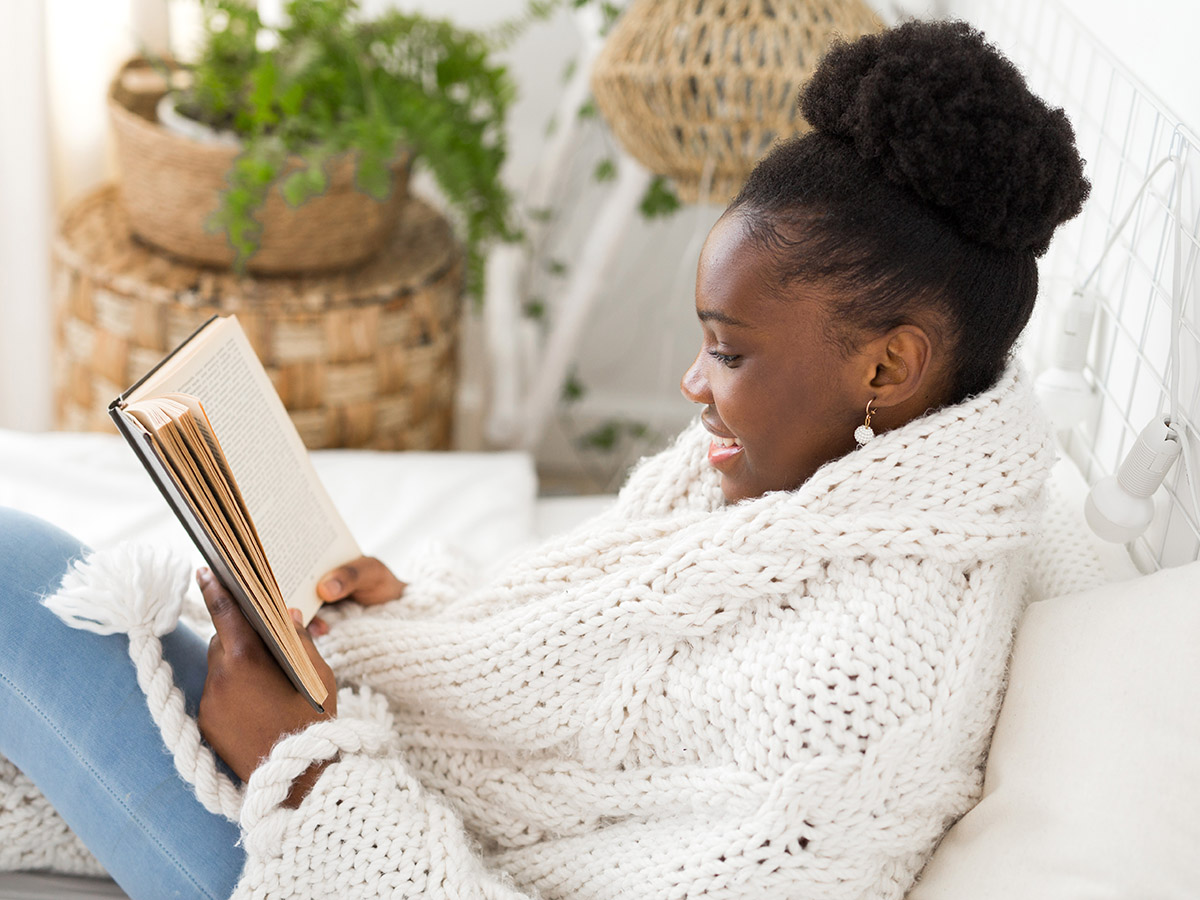 a photo of a student reading a book wrapped in a blanket