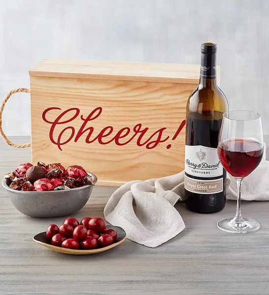 A photo of a picnic with a wooden box that says "cheers" next to a bottle of wine and several bowls of chocolate