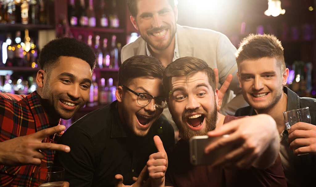 Happy male friends taking selfie and drinking beer