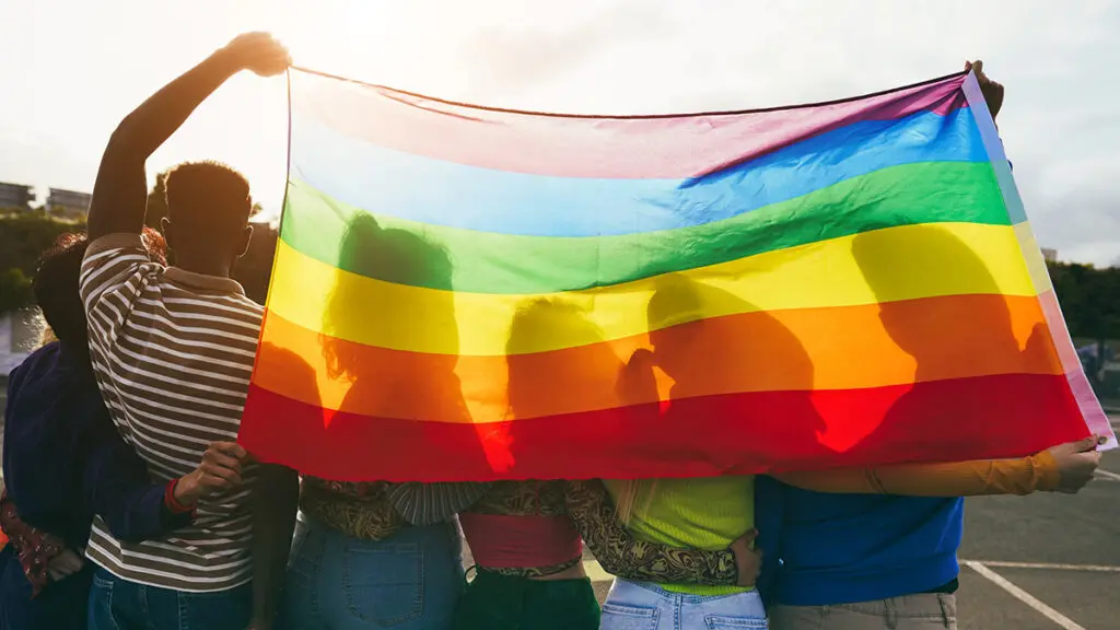 Young diverse people having fun holding lgbt rainbow flag outdoor Main focus on african guy back