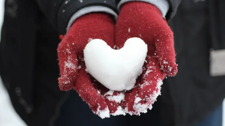 quotes about winter hands wearing red gloves holding a heart-shaped snowball.