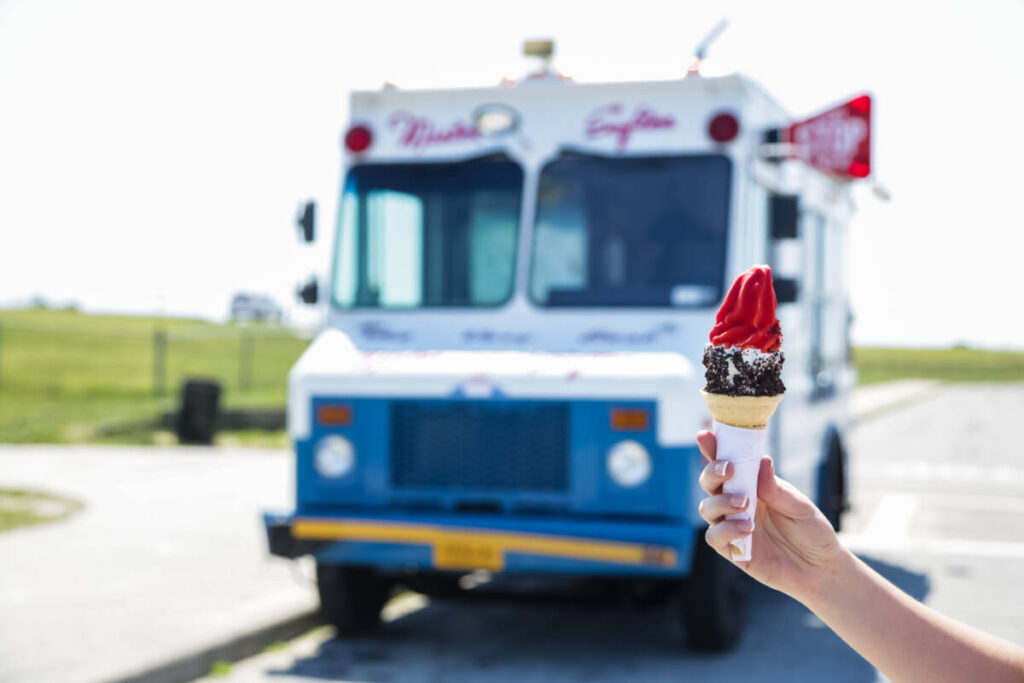 history of ice cream. Person holding an ice cream cone in front of an ice cream truck. 