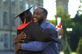 Cheerful father and graduating son hugging outdoor, study achiev