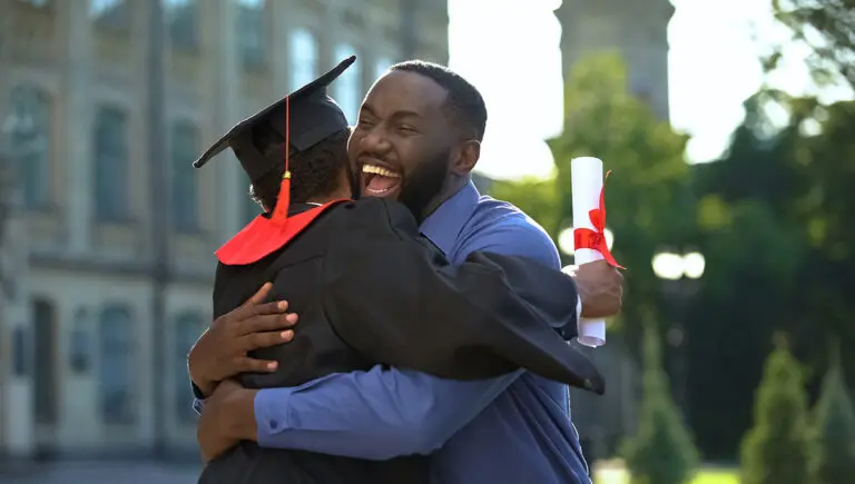 Cheerful father and graduating son hugging outdoor, study achiev